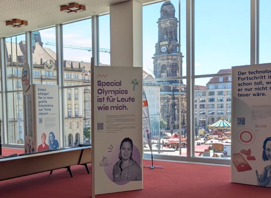 Die Porträtwände im Foyer der Bibliothek. Durch die bodentiefen Fenster ist der Altmarkt mit den Marktständen und der Kreuzkirche zu sehen.